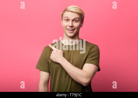 cheerful handsome young man looking at camera ,pointing finger to copy space. close up photo. man shows direction Stock Photo