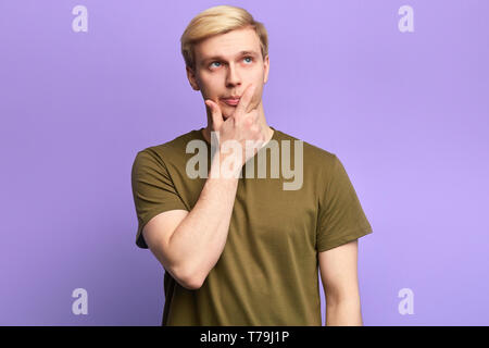 Handsome serious puzzled young man looking up with thoughtful and skeptical expression,solving a aproblem, holding finger on his chin,isolated over vi Stock Photo