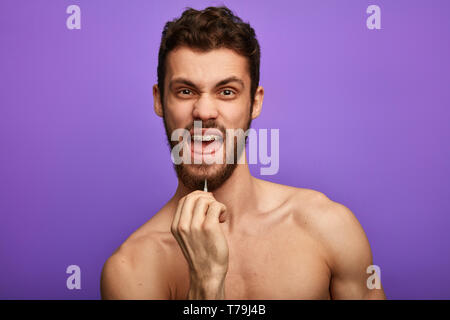 new method of depilation, crazy funny man using tweezers to remove his beard. guy trying to rid of the beard. close up portrait Stock Photo