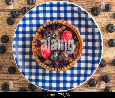 Mixed Berry Tart on a Blue Gingham Plate with a Wood Table Background Stock Photo