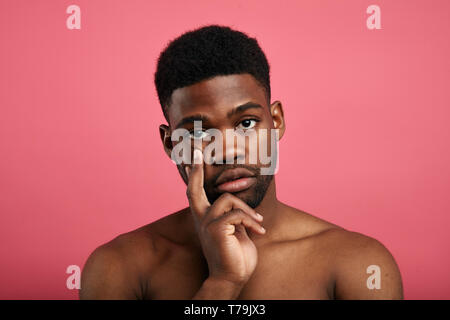 serious young man having concentrated thoughtful expression, keeping her fingers on his chin, isolated over pink background, tiredness Stock Photo