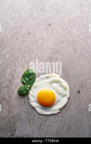 one fried egg with green mint leaf at concrete grey backdrop. minimalistic breakfast concept. vertical. Copy space Stock Photo