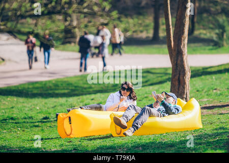 couple laying on yellow inflatable mattress in city park. reading book. drinking smoothies. leisure time Stock Photo