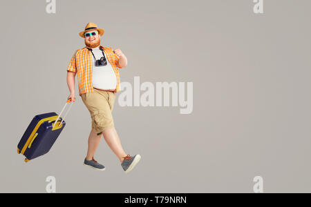 Fat funny man a suitcase smiling goes on a gray background. Stock Photo