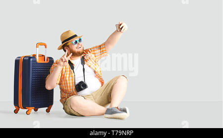 Fat funny man a suitcase smiling goes on a gray background. Stock Photo