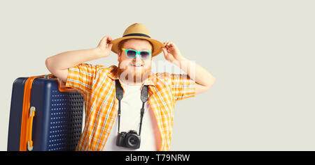 Fat funny man a suitcase smiling goes on a gray background. Stock Photo