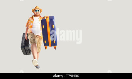 Fat funny man a suitcase smiling goes on a gray background. Stock Photo