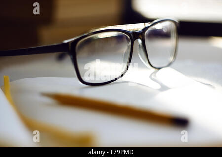 Glasses lying in the workplace, among a notebook, pencil and other items. The light falls on the glasses and is reflected in the stains on the glasses Stock Photo