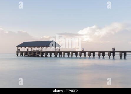 Calm water surrounds the pier at sunrise over Hanalei Pier in Kauai Hawaii with long exposure to smooth the waves to create peaceful scene Stock Photo