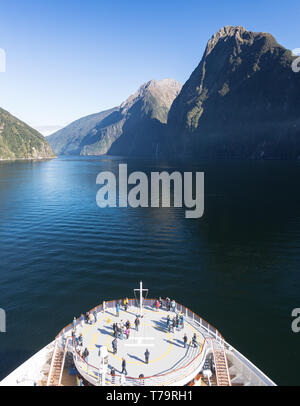 Fjord of Milford Sound in New Zealand with passengers on a cruise ship standing on the bow of the boat and admiring the magnificent scenery Stock Photo