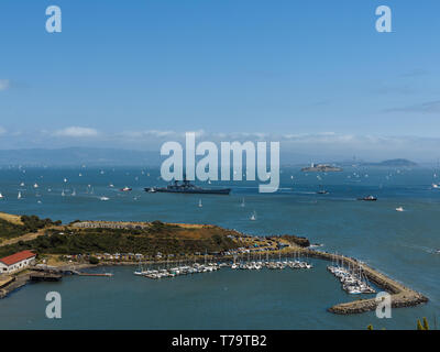 View of San Francisco harbor with hundreds of sailboats dotting water under sail, a navy cruiser, and tugboats leaving bay passing the marina  by the Stock Photo