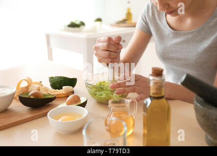 Woman making nourishing mask with avocado in kitchen Stock Photo