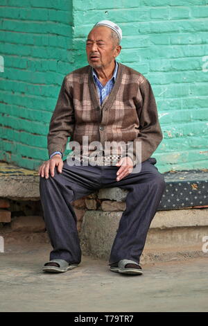 Old Uyghur man on a bench attached to a wall-Hotan-Xinjiang-China-0117 Stock Photo