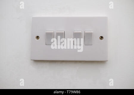 Four way electrical light switch.  White plastic switch with two screws and set agains a white painted wall. Stock Photo