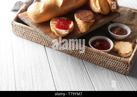 Wicker tray with delicious toasts, jam and chocolate paste on table Stock Photo
