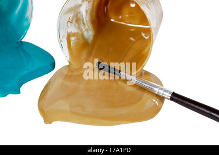 Small bowls of spilled tan and aqua blue acrylic paint laying on its side with an artists paint brush isolated on white Stock Photo