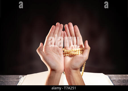 Muslim man praying with prayer beads on his hands in front of the opened quran on wooden table over blurry background Stock Photo