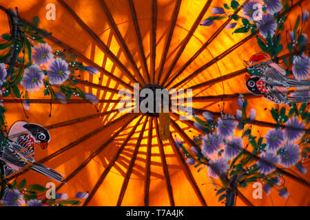 Close up of colorful orange paper umbrella painted with flowers and illuminated by sunlight - Chiang Mai, Thailand Stock Photo