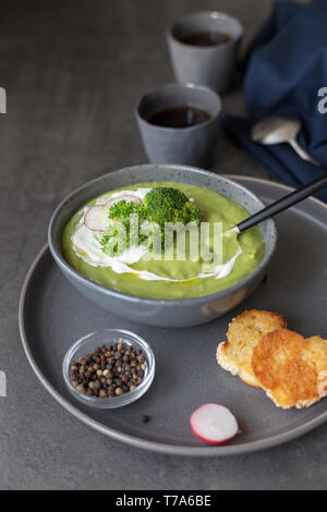 Healthy cream soup with broccoli and sour cream, spoon, pepper and napkin near on concrete gray background. Concept of diet summer food. Side view, sp Stock Photo