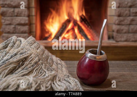 Traditional cup for mate drinking and wool scarf, near cozy fireplace, in country house, hygge, home sweet home. Stock Photo