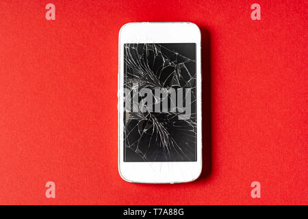 Broken mobile phone with cracked display on red background, flat lay. Stock Photo
