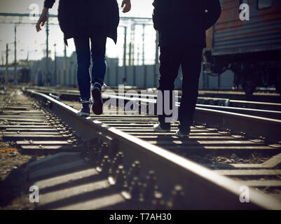 Two carefree and risky teenagers are engaged in dangerous business - go on railway tracks. Stock Photo