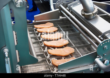 Pieces of meat on a conveyor belt machine dry breading Stock Photo