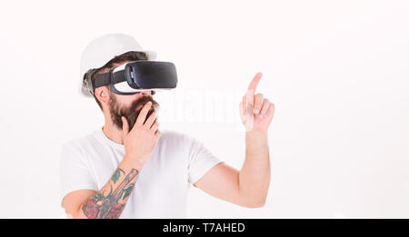 Thoughtful architect making new project using digital touch screen. Builder with beard in helmet isolated on white background. Bearded man in VR glasses having 3D experience, virtual reality concept. Stock Photo