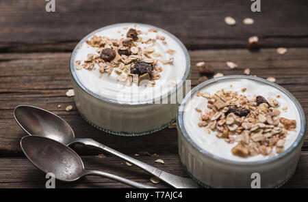 Two glass bowls with white yogurt on old wooden desk with oatmeal on top. Stock Photo