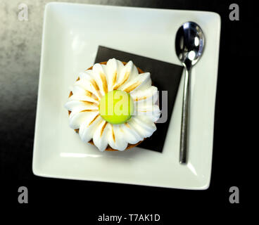 meringue cake on a square plate with a spoon, the table is black and has a green cookie on the meringue Stock Photo