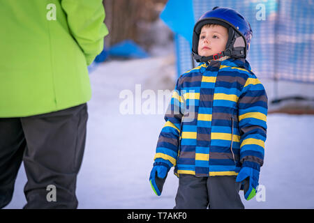 Cute little Caucasian ski adept looking at and listening to his ski instructor on a slope in winter Stock Photo