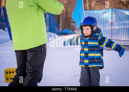 Cute little Caucasian ski adept exercising and listening to his ski instructor on a slope in winter Stock Photo