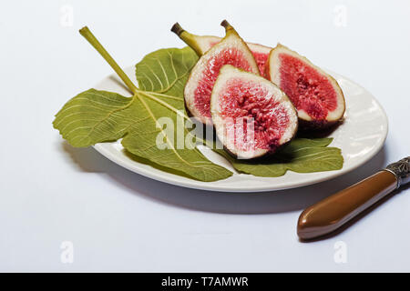 Figs cut in halves on a fig leaf on a white plate Stock Photo