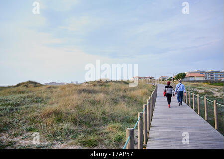 couple walking on the Wooden footwalk over the dunes in portugal near the beach Stock Photo