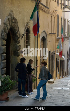 Three girls stand in the street Via Roma Cortona Arezzo Italy