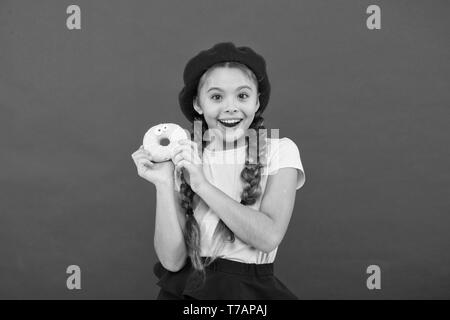 Girl hold glazed cute donut in hand red background. Kid smiling girl ready to eat donut. Sweets shop and bakery concept. Kids huge fans of baked donuts. Impossible to resist fresh made donut. Stock Photo
