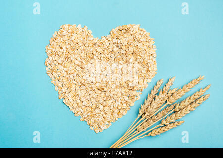 Oats or oat flakes in shape of heart on blue background. Concept of health care, healthy eating, healthy lifestyle and dieting Stock Photo