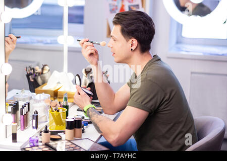 Attentive dark-haired man sitting in front of the mirror Stock Photo