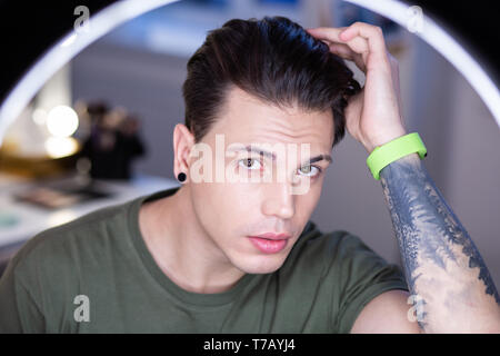 Narcissistic dark-haired young man staying in light circle Stock Photo