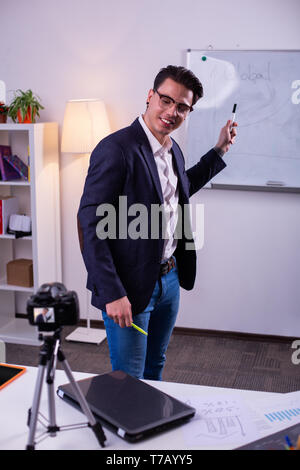 Cheerful positive skilled blogger carrying markers and pointing on graphic Stock Photo