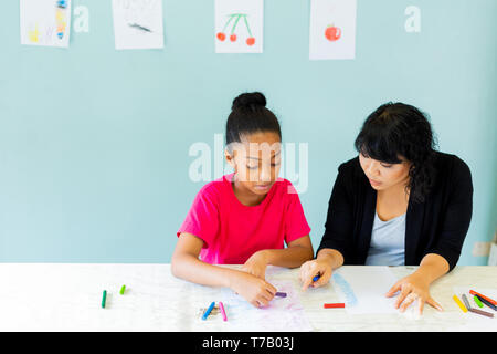 Preteen African American child student learns creative drawing and painting with Asian female teacher and full of crafted art papers Stock Photo