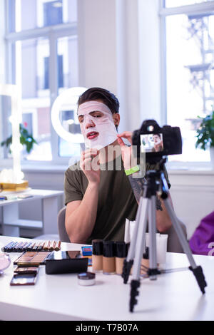 Dark-haired man sitting in front of camera with tripod Stock Photo