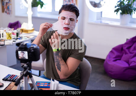 Resolute extraordinary man with tattoos uncovering wet mask Stock Photo