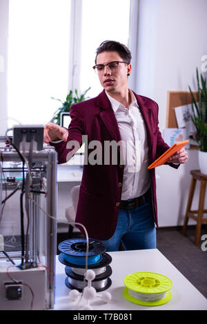 Professional young engineer wearing blue jeans and checking 3d-printer Stock Photo