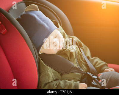 Close Up caucasian cute baby boy sleeping in modern car seat. Child traveling safety on the road. Safe way to travel fastened seat belts in a vehicle  Stock Photo