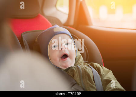 Close Up caucasian cute baby boy woke up and yawns in modern car seat. Child traveling safety on the road. Safe way to travel fastened seat belts in a Stock Photo