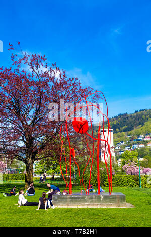 People sitting on grass, having picnic on a sunny day by 'Red Wind' abstract sculpture by Arnold Haukeland (1978) in Bergen, Norway Stock Photo