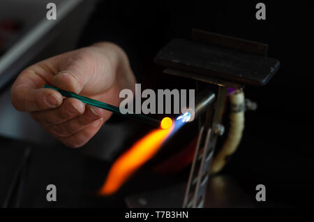 The craftman woman is holding  of a flame and melting glass piece on dark background. Stock Photo