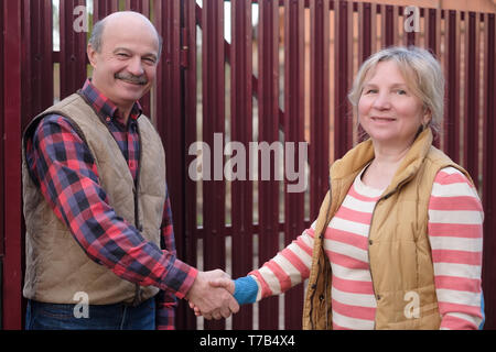 Two senior neighbors takling to each other on sunny day near fence. Stock Photo