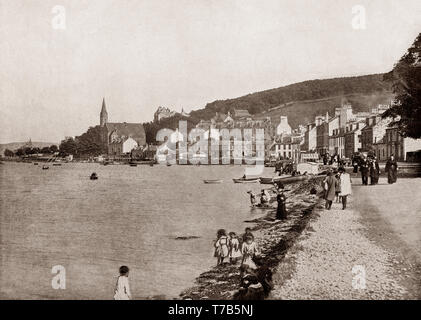 A late 19th Century view of the seafront at Port Bannatyne on the Isle of Bute, Firth of Clyde, Scotland. The village started in 1801 with the building of a small harbour on Kames Bay. Lord Bannatyne of Kames Castle, at the head of the bay, planned the village in an attempt to rival Rothesay. Initially known as Kamesburgh, by the mid-19th century, steamers were calling there regularly. In 1860 the Marquess of Bute purchased this part of the island and renamed the village Port Bannatyne in honour of the long historical association of the Bannatyne family with the area. Stock Photo